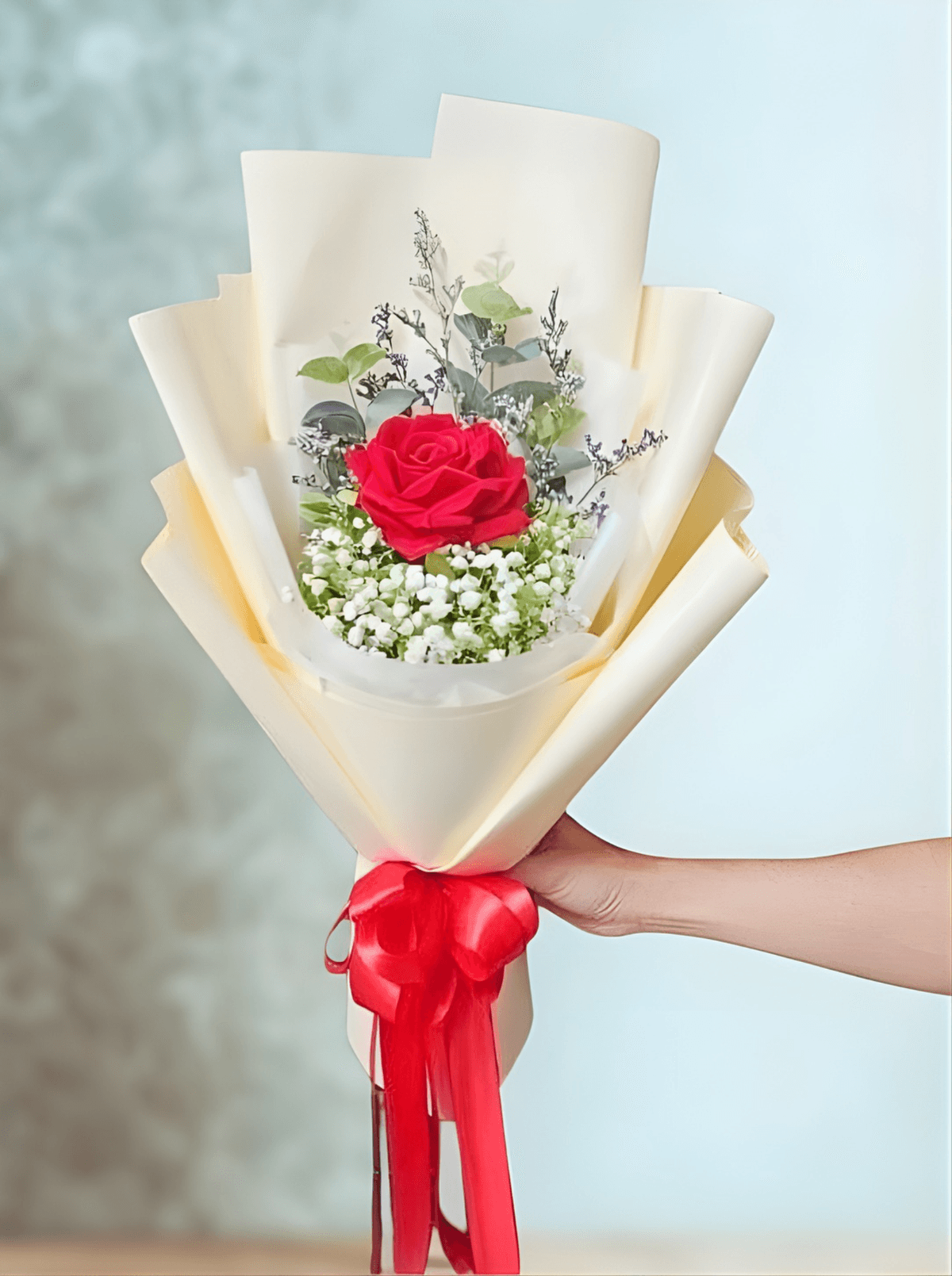 A minimalist single-rose bouquet with a bold romantic feel. One deep red rose stands at the center, softened by delicate white baby’s breath and fresh eucalyptus. Wrapped in clean white paper and finished with a bright red ribbon — simple, elegant, and perfect for a meaningful gesture.